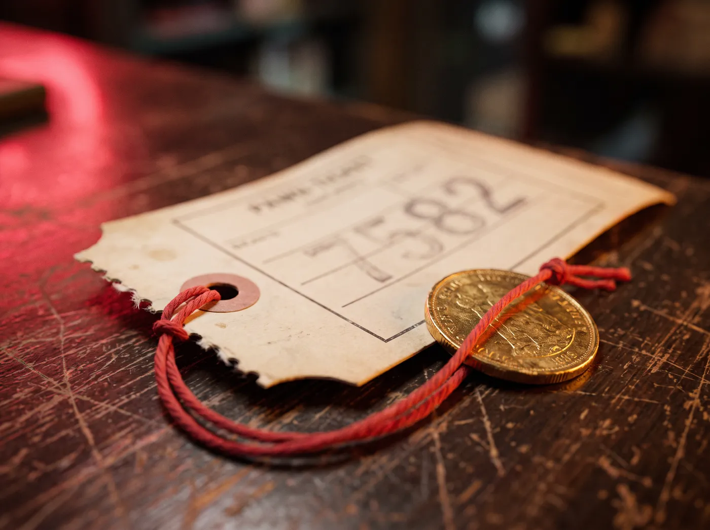A pawn ticket stub tied to a gold coin with red string